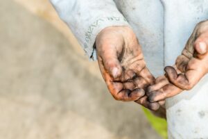 A close-up of a child's hands, caked in black soot and dirt
